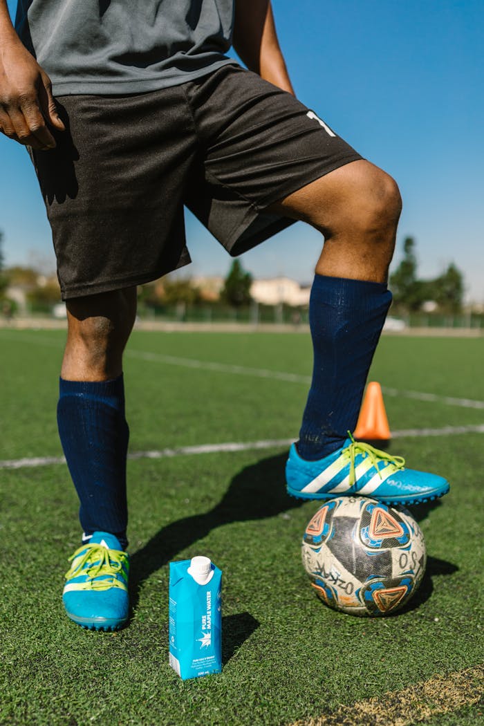 Soccer player preparing for practice on sunny field with ball and water carton.