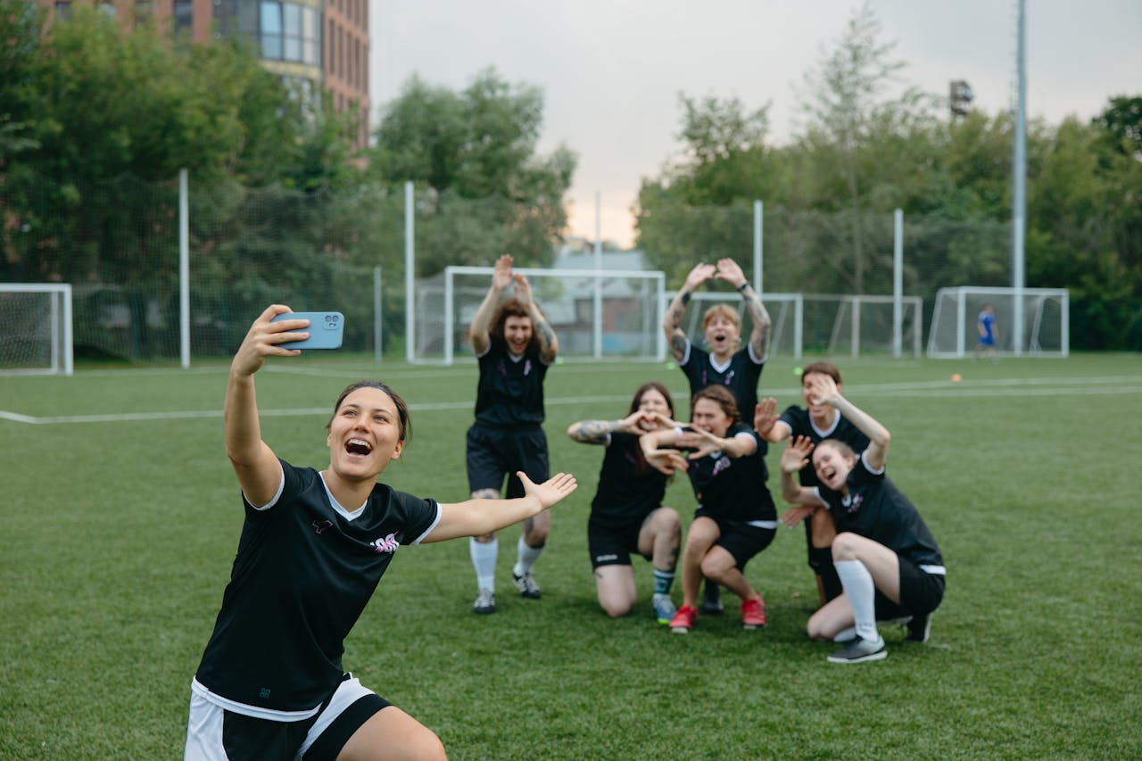 A women's soccer team takes a joyful group selfie on a soccer field, capturing the spirit of teamwork and fun.